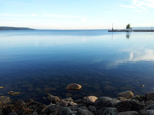 Jönköping pier and rocky beach, blue water reflecting the sky. Photo Vaida Staberg.